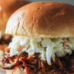 Two slow cooker BBQ pulled chicken burgers topped with coleslaw with pickles and chips.