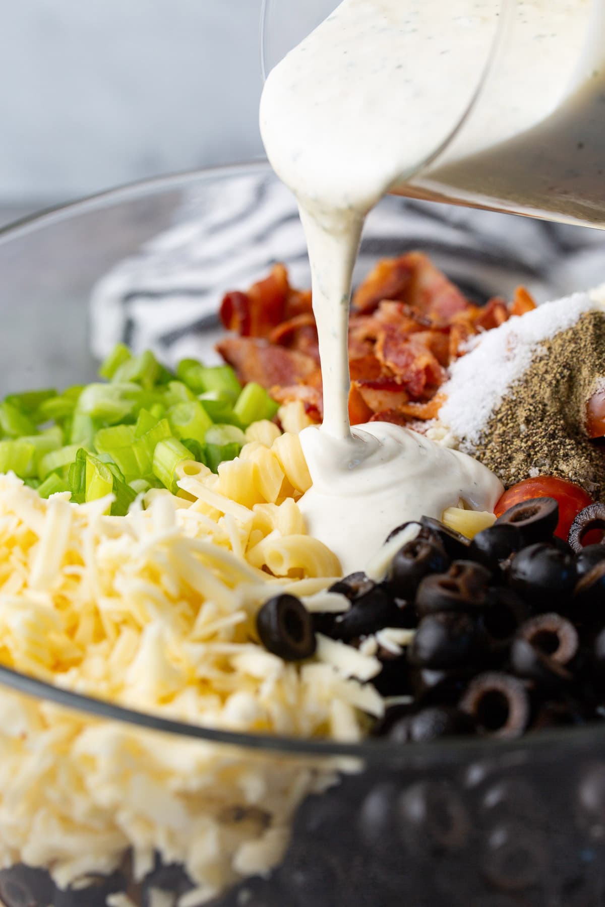 Bacon ranch pasta salad in a large glass mixing bowl with ranch dressing pouring over it.