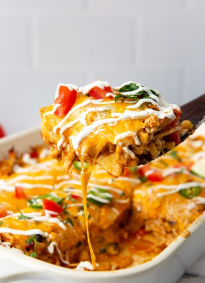 A hearty slice of chicken enchilada casserole lifted out of a white 9x13 casserole pan.