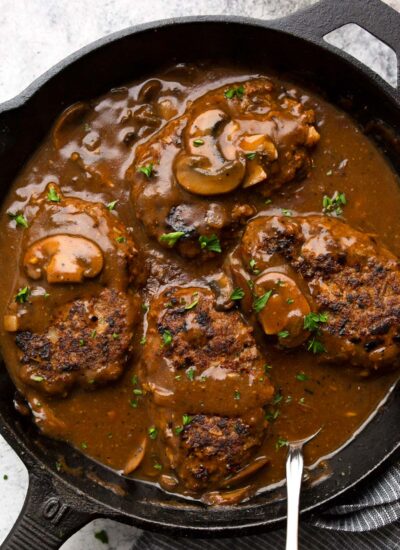 Salisbury steak in a cast iron pan smothered in a mushroom gravy and topped with chopped fresh parsley.