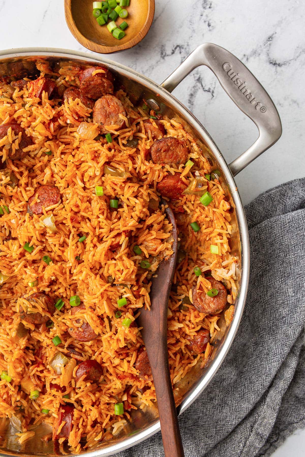 Smoked sausage and rice in a stainless steel skillet topped with sliced fresh green onions.