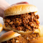 A hand holding a hamburger bun generously stuffed with homemade Sloppy Joes.